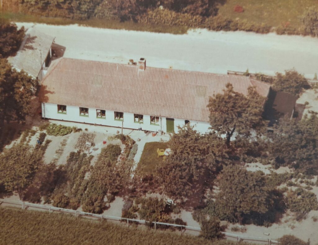 Luftfoto af Vindeholmvej 24 en lang bygning med køkkenhave foran